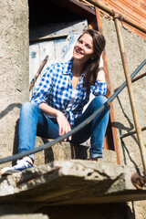 Fototapeta premium Portrait of female wearing jeans and plaid shirt posing at old countryside building