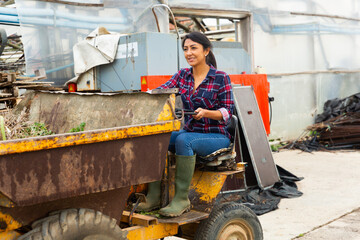 Obraz na płótnie Canvas Latin american woman farmer working at a company driving a mini dump truck takes out to throw out weeds.