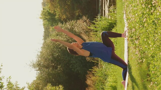 Woman stretching on yoga mat in green park at sunset. Vertical video