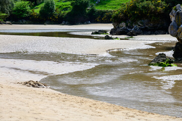 View on Playa de Poo during low tide near Llanes, Green coast of Asturias, North Spain with sandy beaches, cliffs, hidden caves, green fields and mountains.
