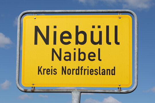 Zweisprachiges Ortsschild (deutsch und nordfriesisch)  von Nieb&uuml;ll bzw. Naibel in Nordfriesland, Schleswig-Holstein, Deutschland, mit blauem Himmel und Wolken.