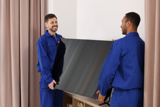 Male movers installing plasma TV near white wall in new house