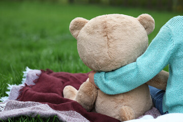 Little girl with teddy bear on plaid outdoors, closeup. Space for text