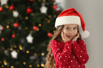 Portrait of cute girl wearing Santa hat at home, space for text. Christmas atmosphere