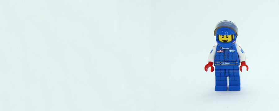 Horizontal banner with a lot of white background and a toy Lego character of a car racer. Racing driver doll. Formula 1 pilot figure with uniform and protective helmet. Copy space for texts.