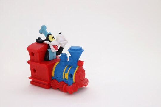 Goofy driving a train in the Disney parks. Disney franchise collectible toy on isolated white background. Happy Goffy in Disneyland attraction.