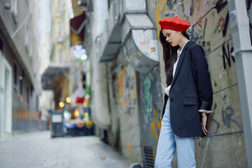 Fashion woman portrait walking tourist in stylish clothes with red lips walking down a narrow city street, travel, cinematic color, retro vintage style, dramatic against a wall with graffiti.