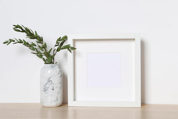 Empty photo frame and vase with decorative leaves on white table. Mockup for design