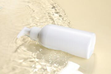 Bottle of face cleansing product in water against beige background