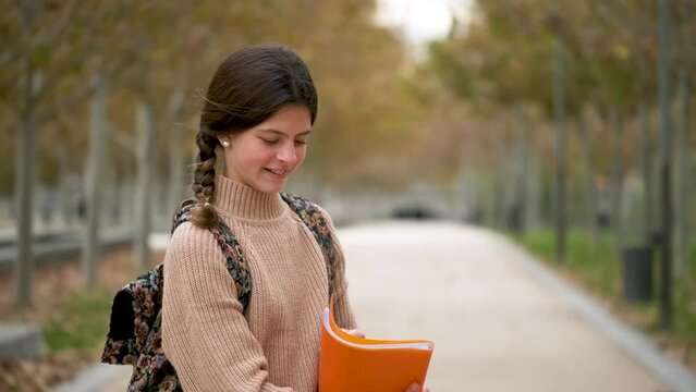 Preteen girl with two braids, grabbing a folder smiling and looking at camera outdoors in autumn. Back to school.