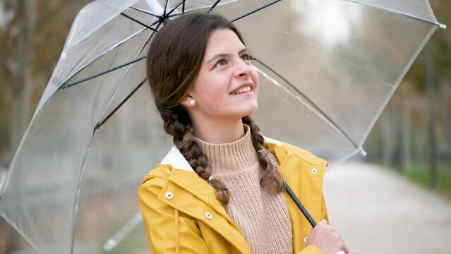 Portrait of preteen girl in yellow raincoat opening an umbrella, smiling and looking at camera outdoors in autumn.