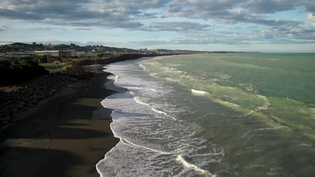 Drone flyover black sand beach reveal seafront of Oamaru town, New Zealand landscape.