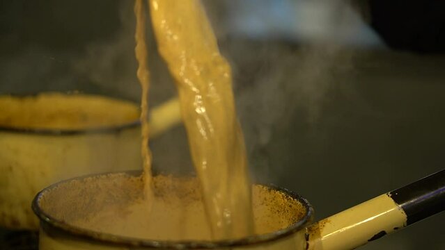The tea is cooked on a low flame and the tea maker is stirring it with a spoon in Lahore Pakistan - Queta Tea