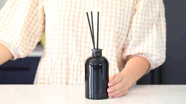 A woman inserts wooden sticks into a diffuser with a fragrance for the house.