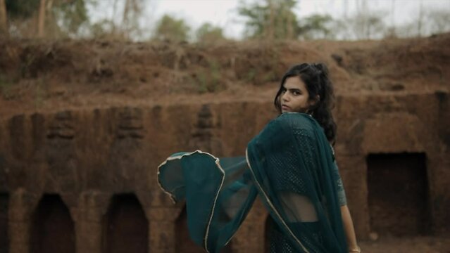 Indian woman in purple indian lehenga choli dress and shawl swings arm in ruins