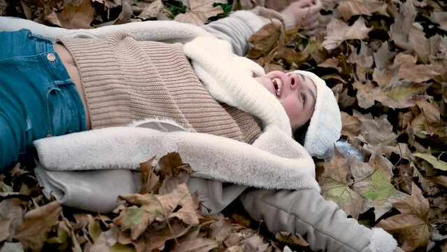 Preteen girl lying down on the ground playing with fallen leaves during autumn season. Happiness.