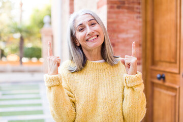 senior retired pretty white hair woman feeling awed and open mouthed pointing upwards with a shocked and surprised look