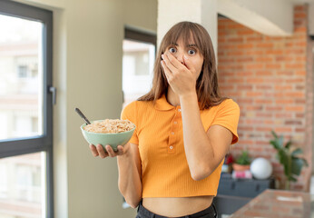 young pretty woman covering mouth with a hand and shocked or surprised expression. breakfast bowl concept