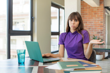 young pretty woman shrugging, feeling confused and uncertain.  universitary student with a laptop