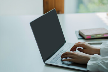 Young woman online job hunting working with laptop computer, blank screen at desk and close up working with computer hands.