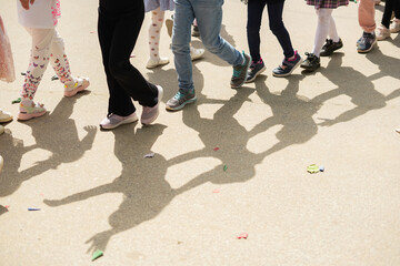 Group of unrecognizable kids in casual summer clothes walking in a column on asphalt road. Cropped shot, kids' legs. Leisure lifestyle concept. Summer activity