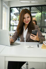 A businesswoman checking messages on her smartphone while sitting at her desk
