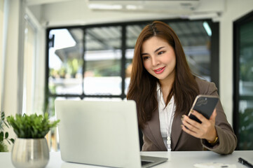 A businesswoman holding her smartphone while working on her work on laptop