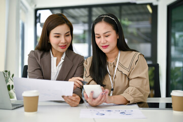 Businesswomen are rechecking sales data with calculator and analyzing financial data reports