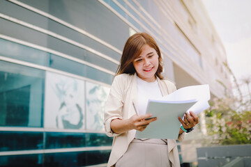 Stylish business woman holding documents in hand  walking around town near office towers, working outside.