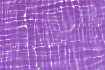 Purple water with ripples on the surface. Defocus blurred transparent pink colored clear calm water surface texture with splashes and bubbles. Water waves with shining pattern texture background.