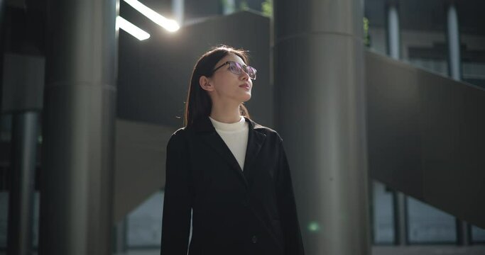 Footage of Young Asian busy businesswoman wearing glasses in a suit with crossed arms looking at the camera while standing in a modern business building. Business and people concepts.