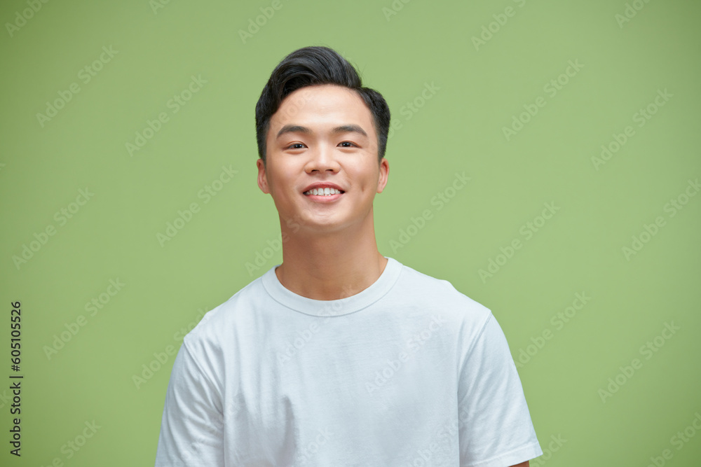 Wall mural Close up portrait of smiling handsome man in white t-shirt looking at camera, isolated on green background