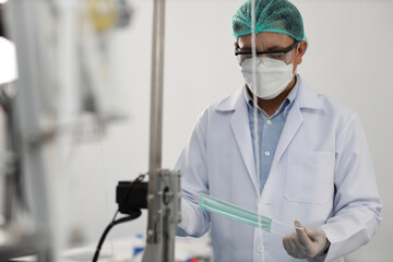 Worker in personal protective equipment or PPE inspecting quality of mask and medical face mask production line in factory, manufacturing industry and fac