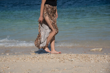 Young girl walking at the beach in summer vacation. Stylish happy woman wears in leopard pant having fun on the tropical beach with copy space. Close up of legs.