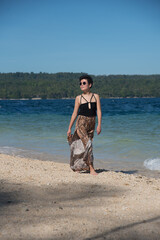Pretty asian girl walking near the sea in summer vacation. Stylish pretty woman with short black hair wears in leopard long skirt having fun on the tropical beach. Copy space and blue sky.