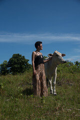 Pretty female model posing in leopard clothes with cow. Woman wears short black hair and sunglasses. Concept - tourism, travel, vacation, friendship, farm animals. Blue sky