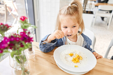 Cute little girl drinking eating rice porridge with mango. enjoying breakfast. Kid having breakfast at cafe. 