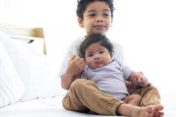 Fototapeta premium Happy boy feeding his newborn sister from a bottle on bed at home, Family love