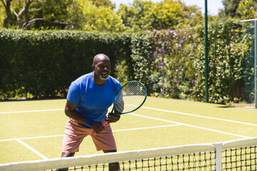 Happy senior african american man playing tennis on sunny grass court