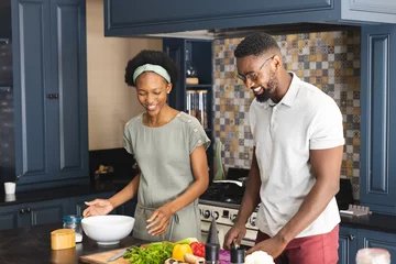 Schilderijen op glas Happy african american couple cutting vegetables, preparing meal together in kitchen © WavebreakMediaMicro