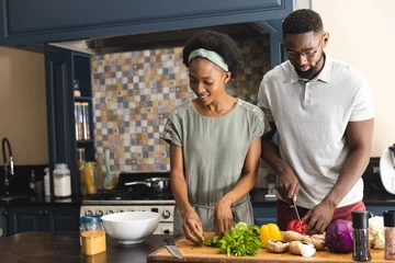 Tuinposter Happy african american couple cutting vegetables, preparing meal together in kitchen © wavebreak3