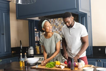 Fotobehang Happy african american couple cutting vegetables, preparing meal together in kitchen © wavebreak3