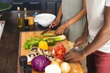 Tuinposter Hands of african american couple cutting vegetables, preparing meal together in kitchen © wavebreak3