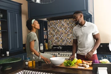 Tuinposter Happy african american couple talking and preparing meal together in kitchen © wavebreak3