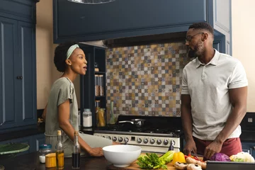 Tuinposter Happy african american couple talking and preparing meal together in kitchen © WavebreakMediaMicro