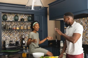 Tuinposter Happy african american couple talking and preparing meal together in kitchen © wavebreak3