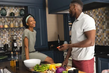 Tuinposter Happy african american couple talking and preparing meal together in kitchen © WavebreakMediaMicro