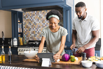 Happy african american couple preparing meal together using tablet in kitchen