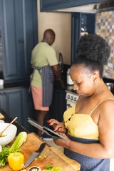 Tuinposter Focused senior african american couple preparing meal together, using tablet in kitchen © WavebreakMediaMicro