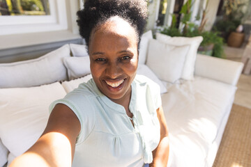 Portrait of happy senior african american woman smiling during video call in sunny living room